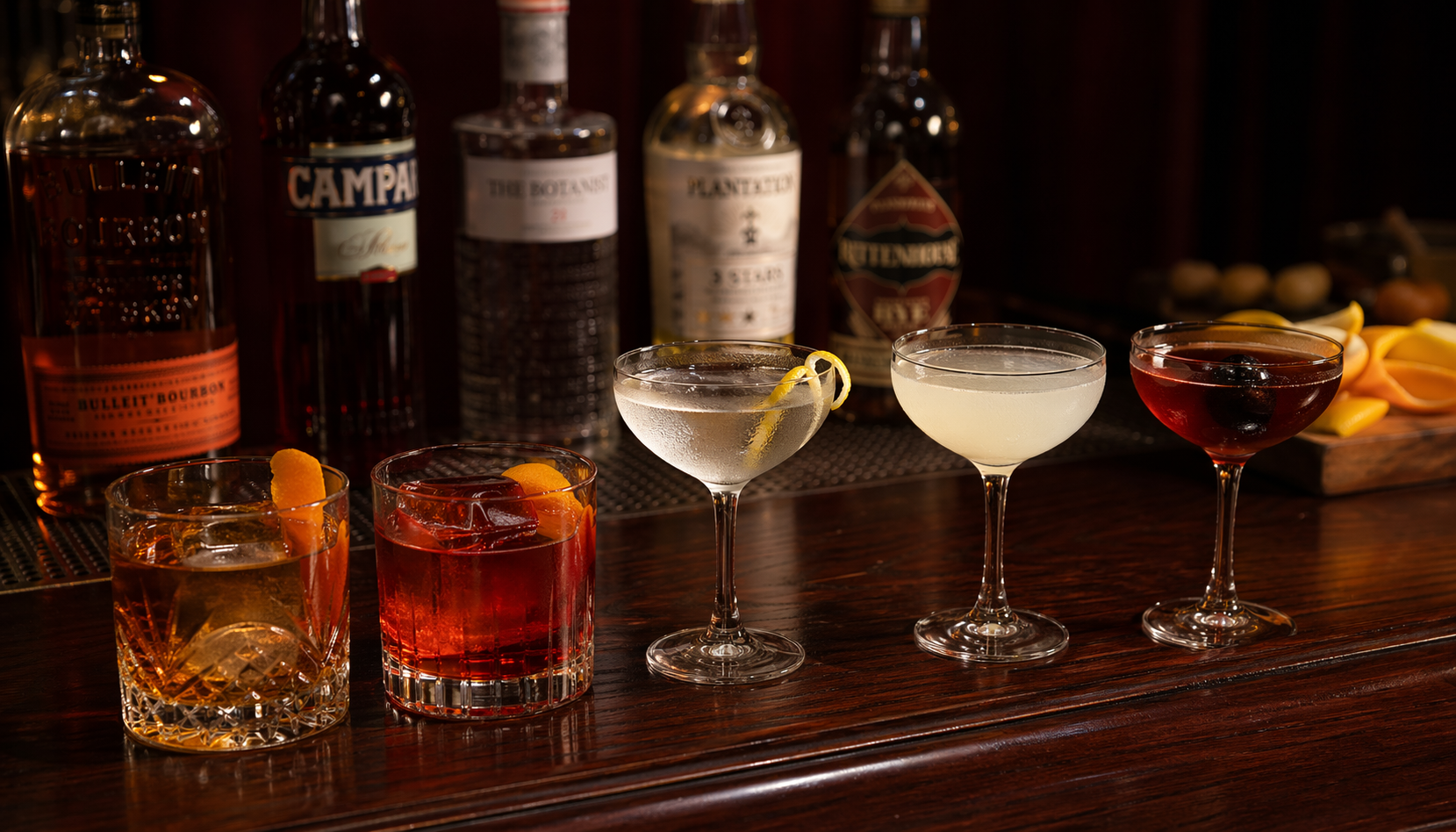 Five classic cocktails arranged in a row on a dark mahogany bar